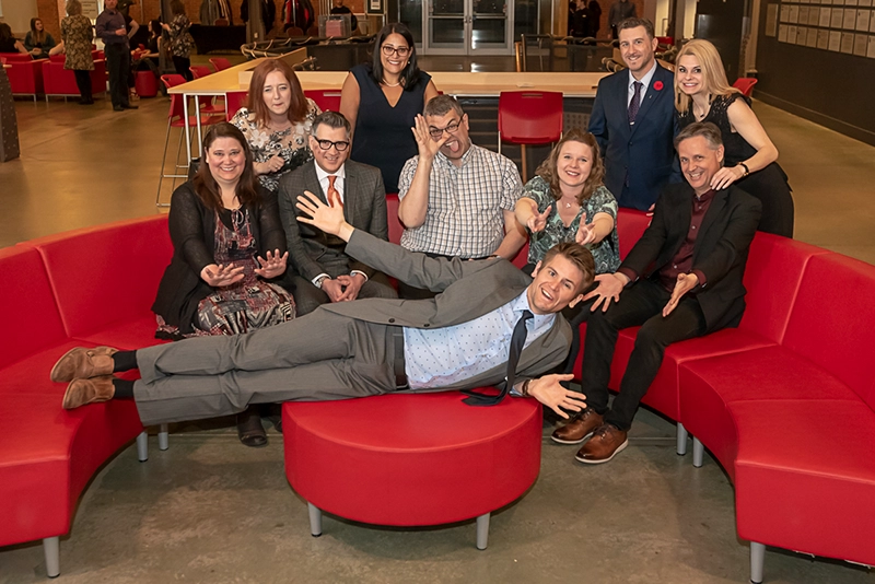 A group of people posing together at an event at Pier 21 in Halifax. The individuals are dressed in formal or business attire, with the historic Pier 21 building and waterfront visible in the background. The photo captures a lively and professional atmosphere during the event.