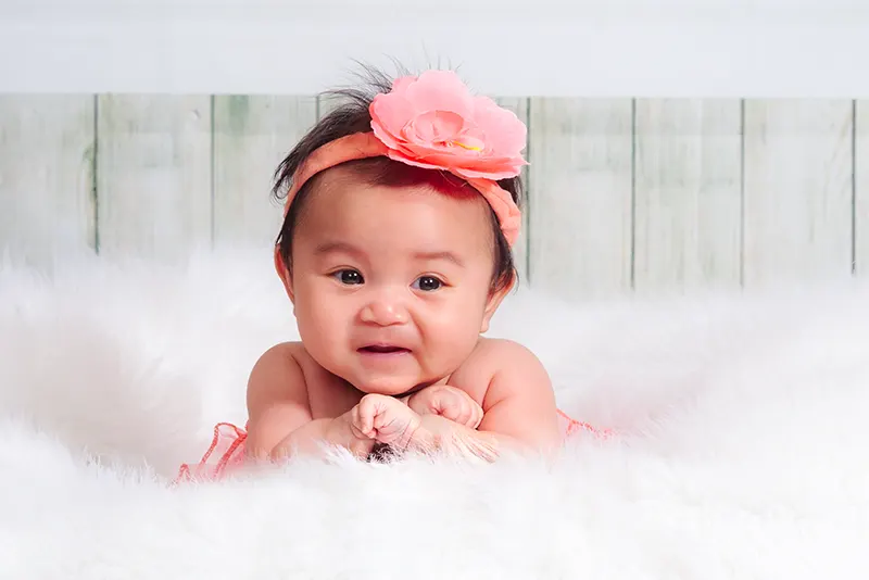 Studio infant portrait of a baby girl wearing a pink flower headband on a white faux fur backdrop by Moments in Time Photography Studio Halifax