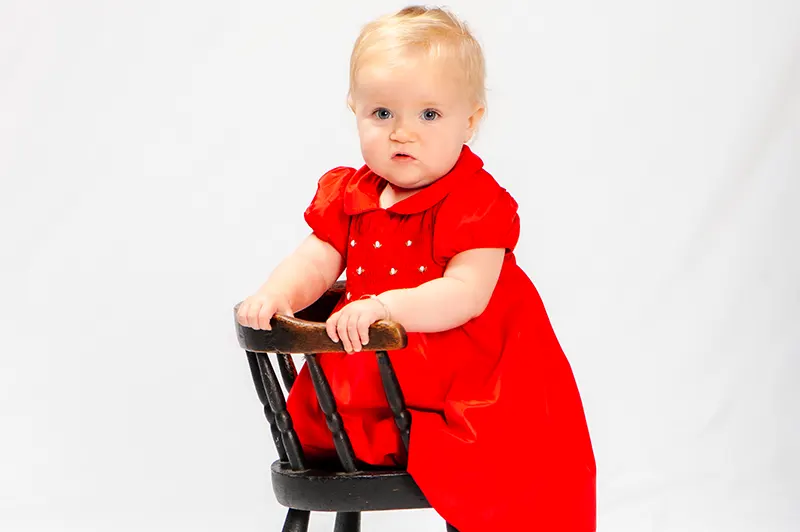Studio portrait of a blonde baby girl wearing a vibrant red dress on a high-key background by Moments in Time Photography Studio Halifax