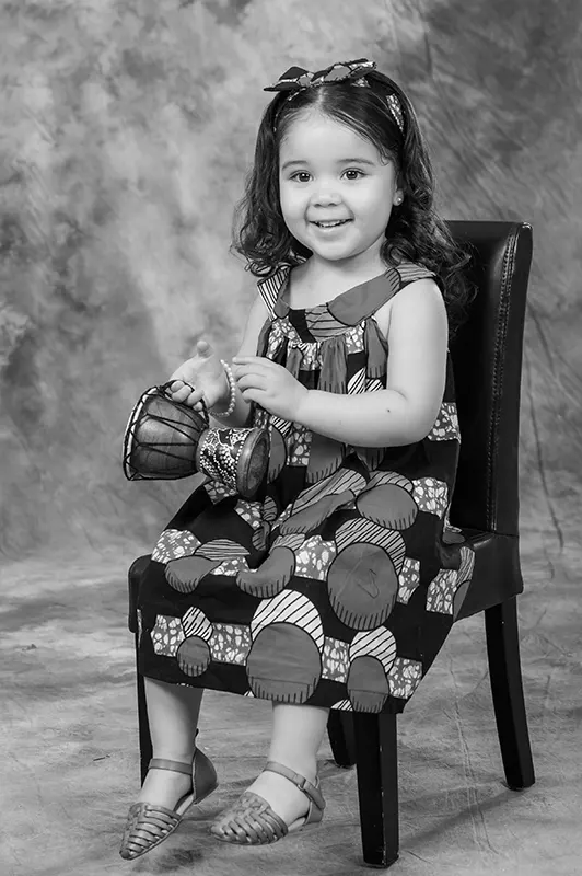 Black and white studio portrait of a smiling young girl holding a miniature drum by Moments in Time Photography Studio Halifax