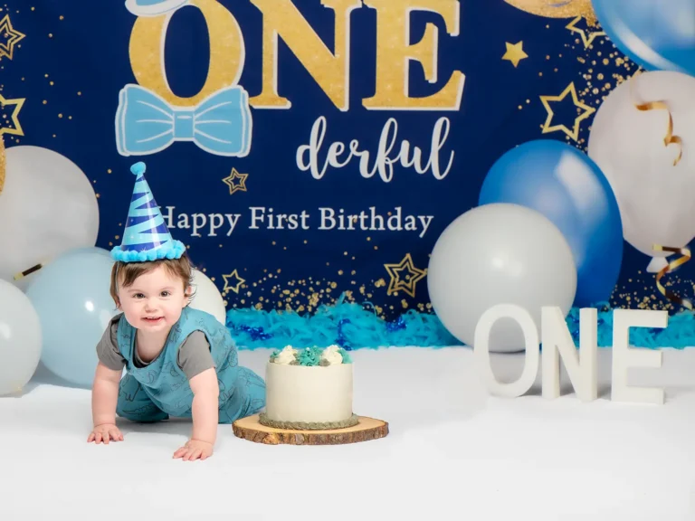 Halifax Photographers & Photography Studio 4 Baby boy in blue party hat crawling beside a small cake in front of a navy and gold ONEderful first birthday backdrop at a Halifax cake smash session