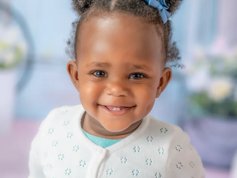 Halifax Photographers & Photography Studio 5 Smiling toddler girl with blue hair bow and white cardigan in a bright children's portrait taken at a Halifax photography studio