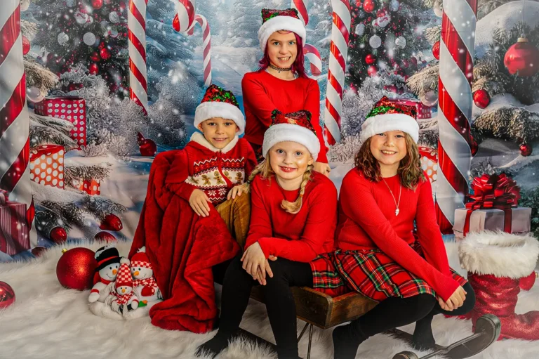 Christmas mini portrait sessions Halifax Nova Scotia 2 Four siblings in red outfits and sequin Santa hats on a sleigh with a candy cane backdrop, Halifax Christmas family portrait