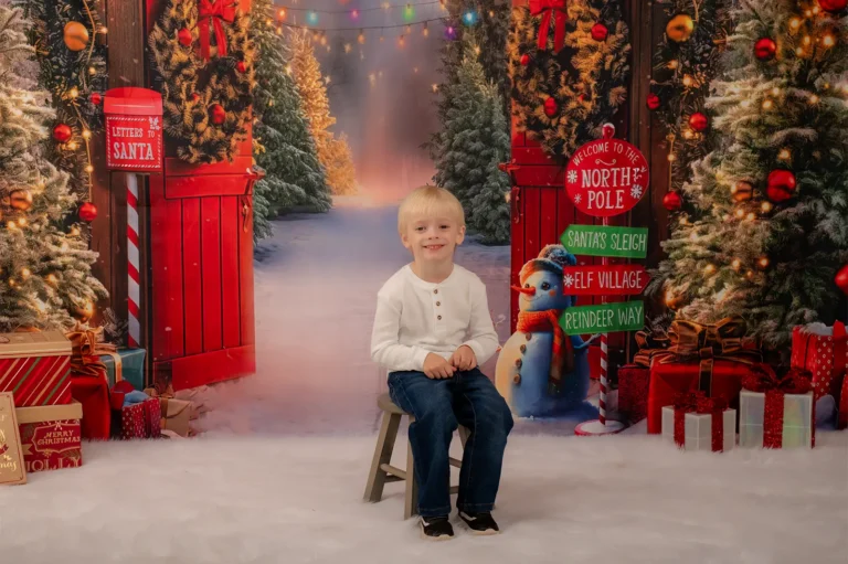 Christmas mini portrait sessions Halifax Nova Scotia 7 Smiling boy in a white shirt and jeans sitting on a stool in front of a North Pole sign and snowman, Halifax Christmas mini session