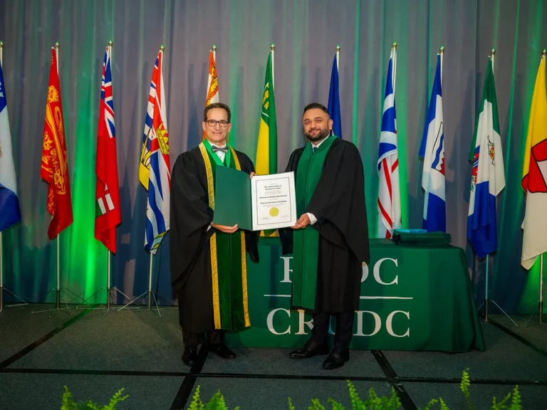 Halifax Photographers & Photography Studio 9 Two people in academic gowns holding a certificate in front of Canadian provincial flags at a professional awards ceremony in Halifax