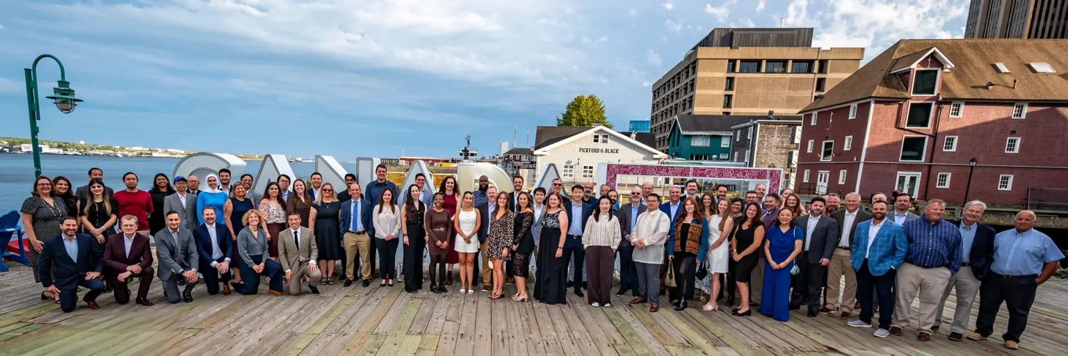 Halifax Photographers & Photography Studio 8 Large corporate group of over 100 people posing together on the Halifax waterfront boardwalk in front of the CANADA sign and harbour