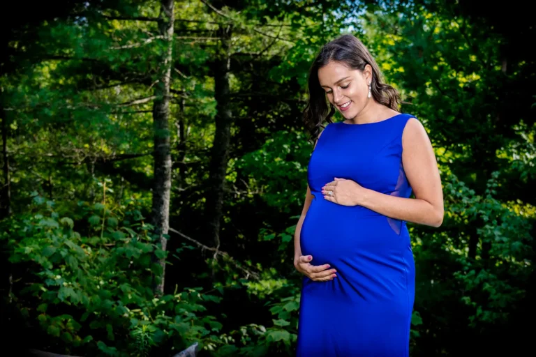 Maternity Portraits 4 Pregnant woman in a royal blue gown holding her baby bump among green trees, outdoor maternity portrait in Halifax