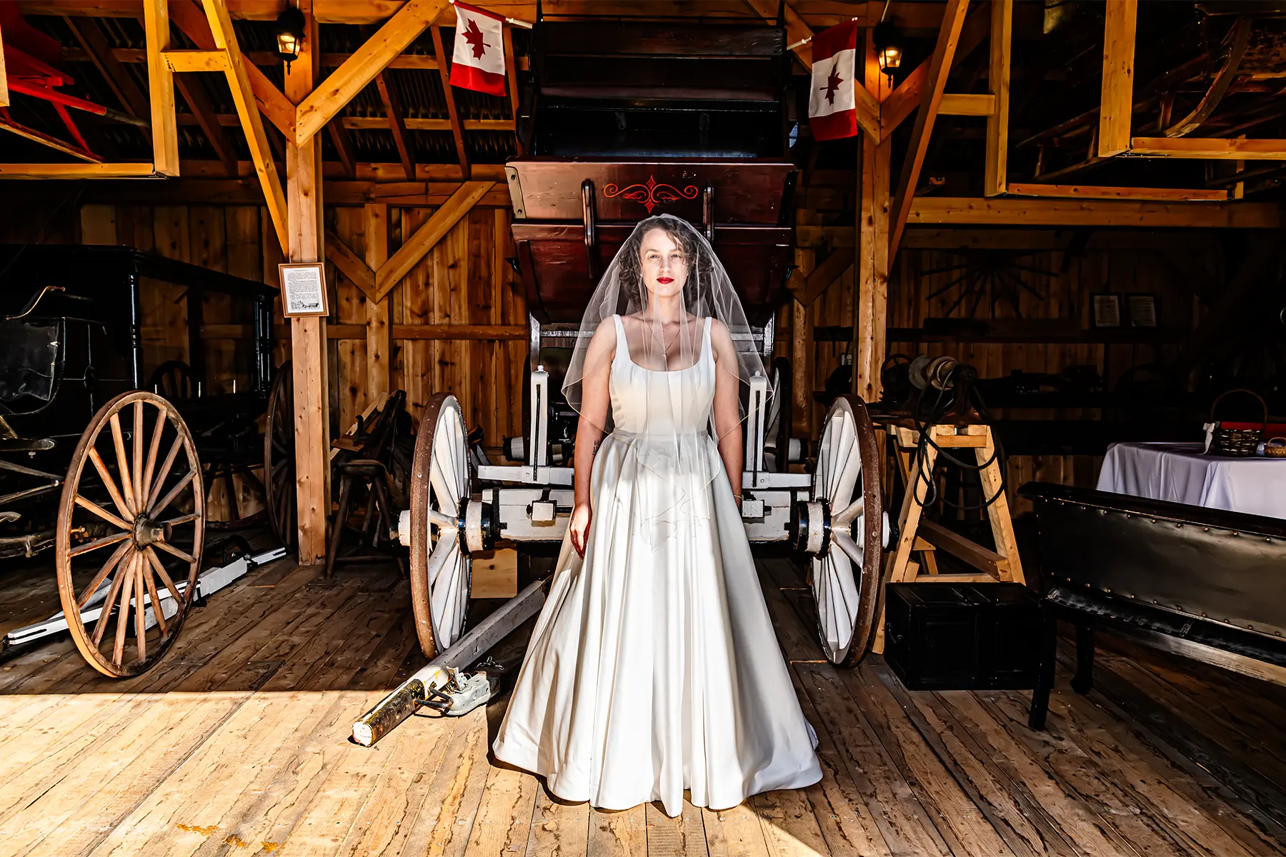 Wedding Photography 1 Halifax wedding photographer portrait of a bride in a white gown and veil standing in front of a vintage carriage in a historic wooden barn