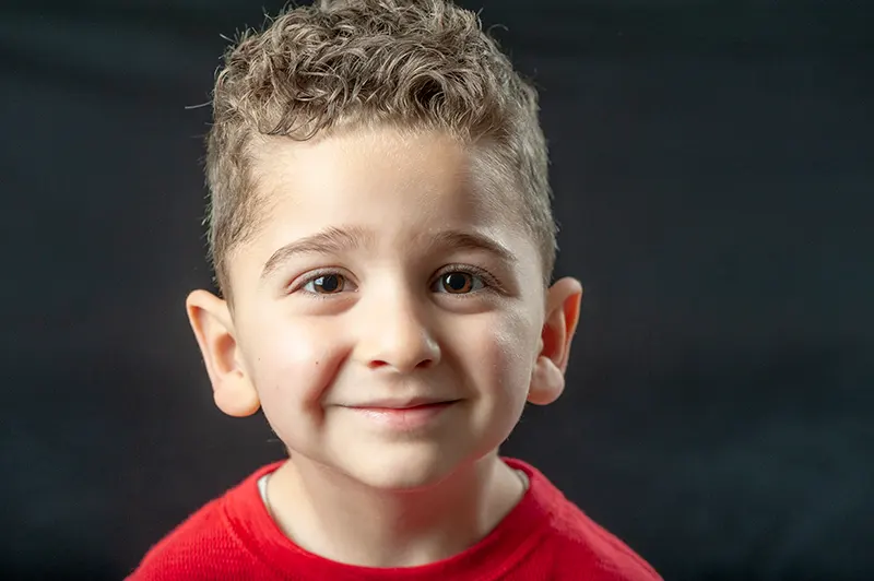 Close-up studio headshot of a smiling young boy with curly hair on a dark backdrop by Moments in Time Photography Studio Halifax