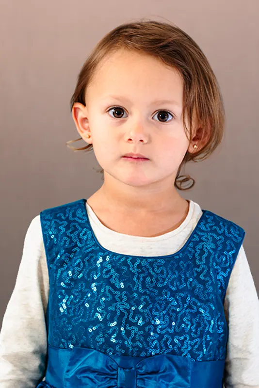 Studio portrait of a young girl wearing a blue sequined dress against a textured gray background by Moments in Time Photography Studio Halifax